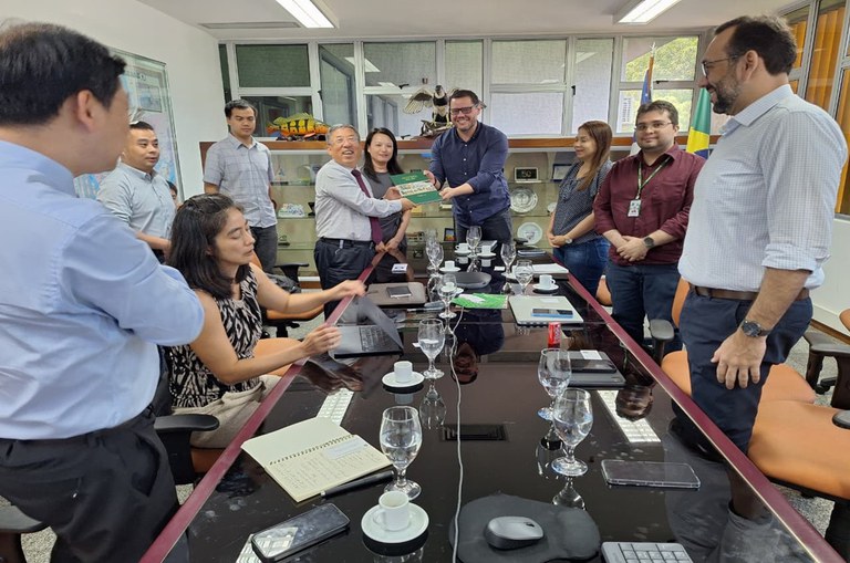 Foto mostra dois homens segurando um livro, observados por grupo de pessoas