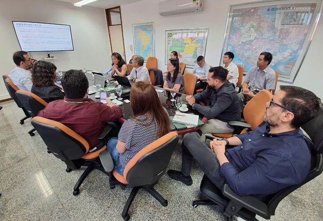 Foto mostra pessoas olhando para um telão durante explanação numa reunião