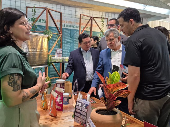 Foto mostra homens olhando para produtos, artendidos por mulher tatuada