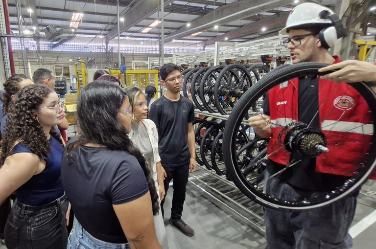 Foto mostra homem mostrando roda de bicicleta a jovens estudantes