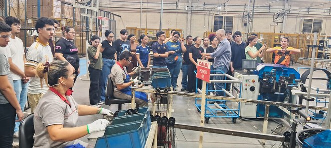 Foto mostra jovens visitando linha de produção de fábrica de bicicleta