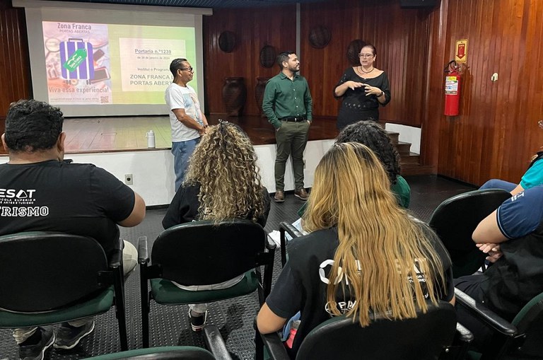 Foto mostra vestida com roupa preta fazendo uma explicação a um grupo de pessoas