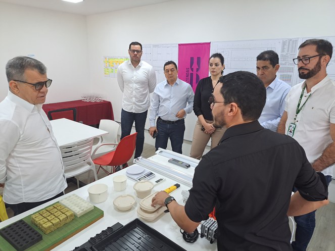 Foto mostra homem de blusa preta mostrando produtos a visitantes