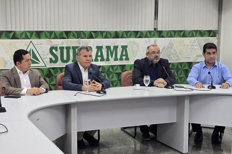 Foto mostra homem falando ao microfone ao lado de outros três homens