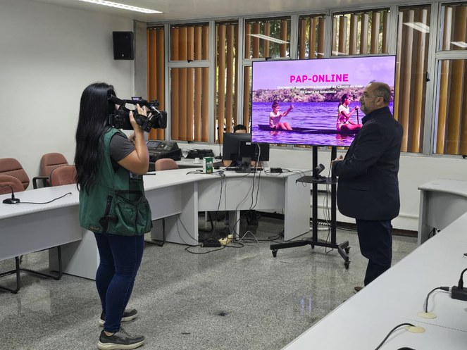 Foto mostra mulher filmando um homem com uma câmera e um telão de fundo