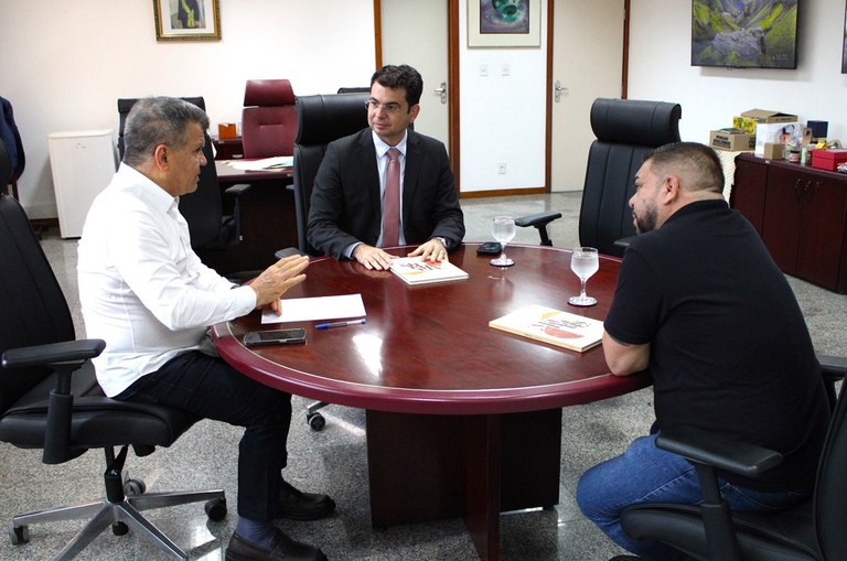 Imagem com três pessoas ao redor de uma mesa redonda em reunião