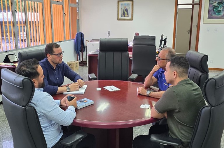 Foto mostra quatro homens numa reunião e um quadro ao fundo