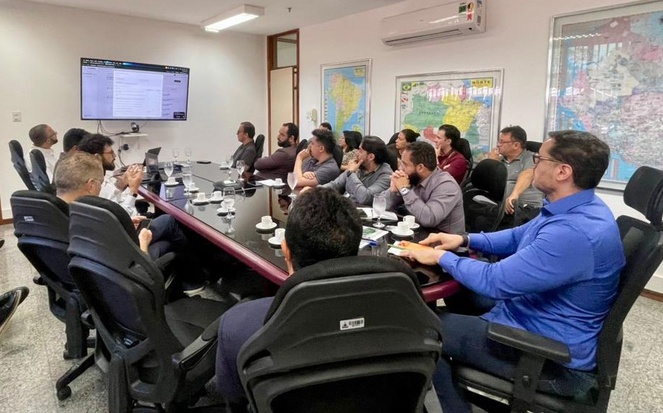 Foto mostra grupo de pessoas em reunião numa sala fechada