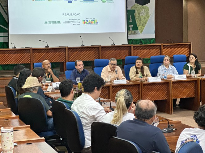 Foto mostra homem falando ao microfone num auditório e com um painel grande ao fundo