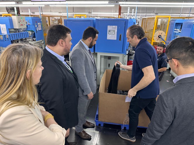 Foto mostra homem vestido de blusa azul mostrando fiação a um grupo de pessoas