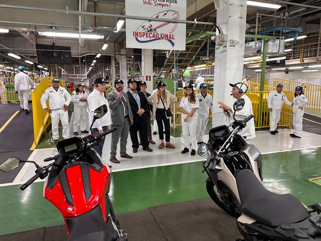 Foto mostra grupo de pessoas em visita a um fábrica de motos