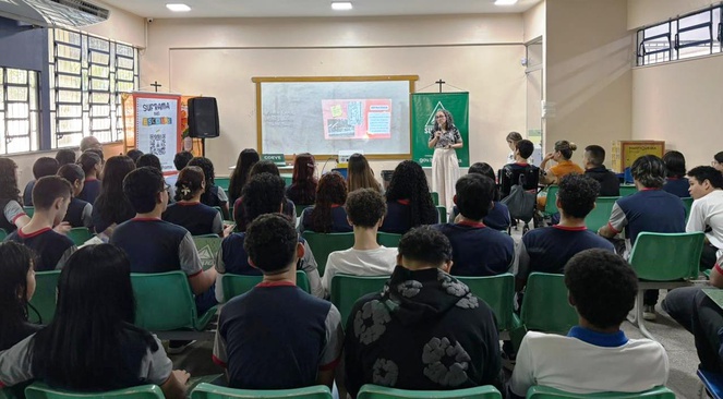 Foto mostra uma mulher fazendo uma palestra para uma sala com alunos