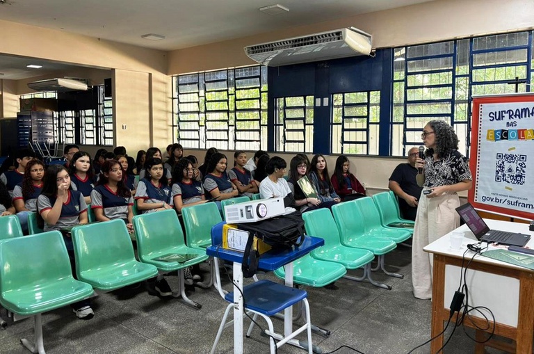 Foto mostra mulher fazendo uma palestra para uma sala com alunos