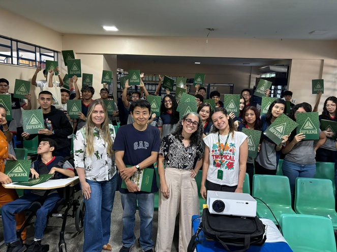 Foto mostra pessoas em pé numa sala e com pastas de papel nas mãos