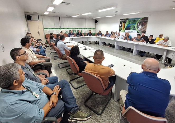 Foto mostra grupo de pessoas observando a fala de um homem vestido de paletó