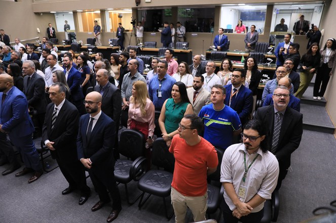Foto mostra pessoas em posição de cantar o Hino Nacional