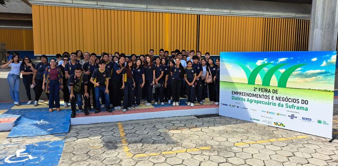 Foto mostra grupo de estudantes posando para sessão de foto ao lado de uma placa