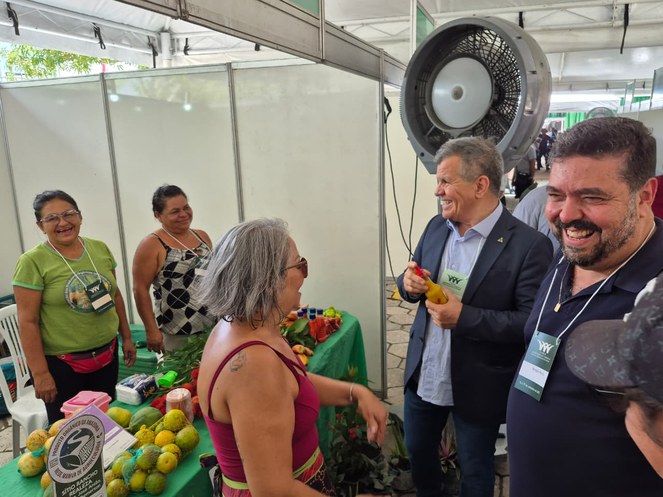 Foto mostra homem segurando objeto e rindo, com outras pessoas