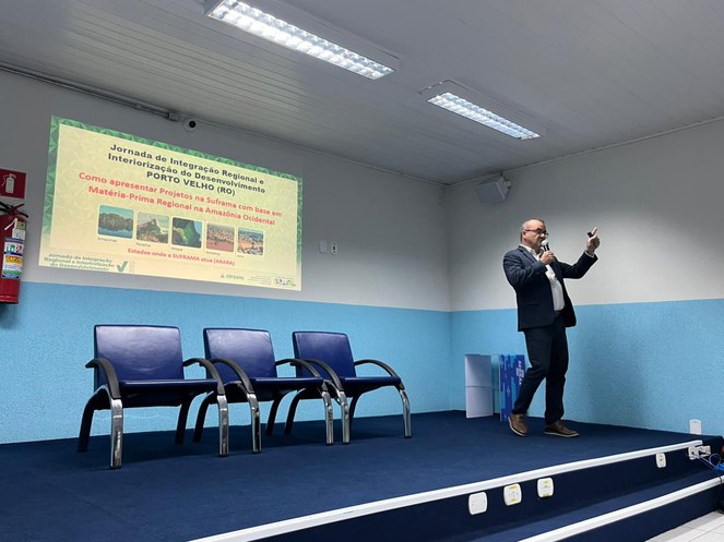 Foto mostra homem falando num evento com telão ao fundo