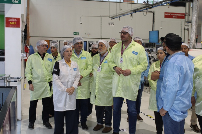 Foto mostra grupo de pessoas de jaleco e boné olhando para equipamentos eletrônicos