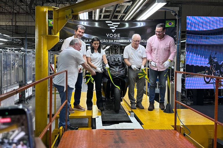Foto mostra grupo de pessoas cortando faixa de inauguração dentro de uma fábrica de motocicletas