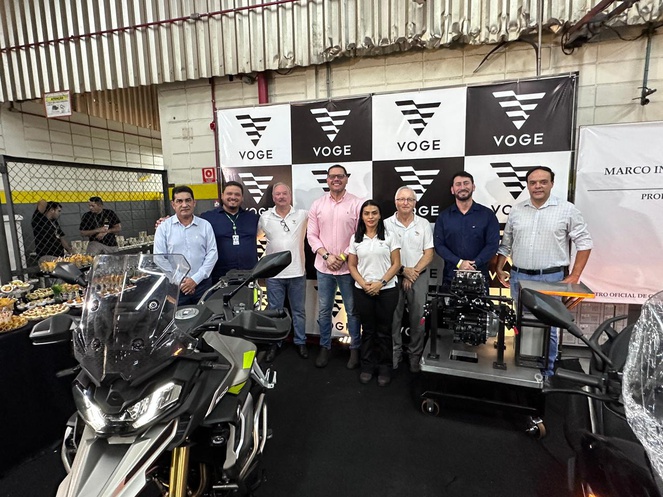 Foto mostra grupo de pessoas posando para sessão de foto dentro de uma fábrica de motocicletas
