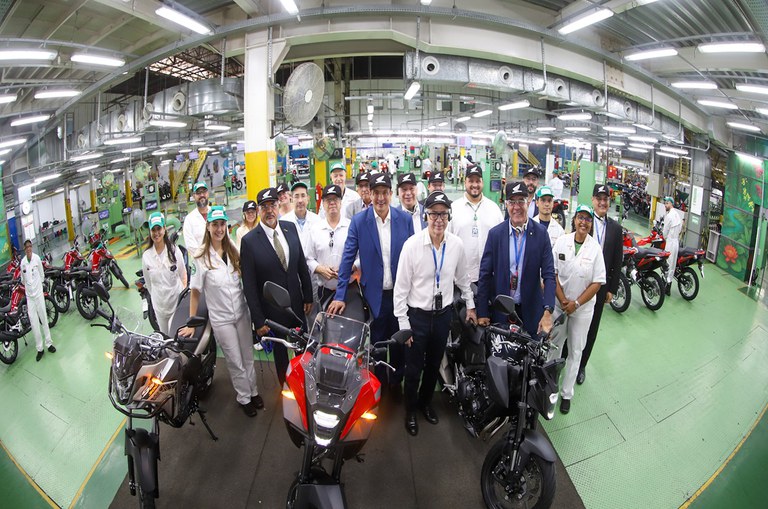 Foto mostra grupo de pessoas reunidas para foto, cercadas de motocicletas
