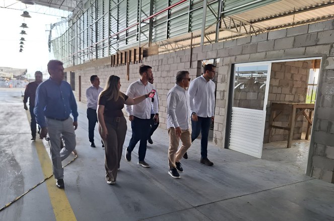 Foto mostra mulher apontando para uma parede em obra