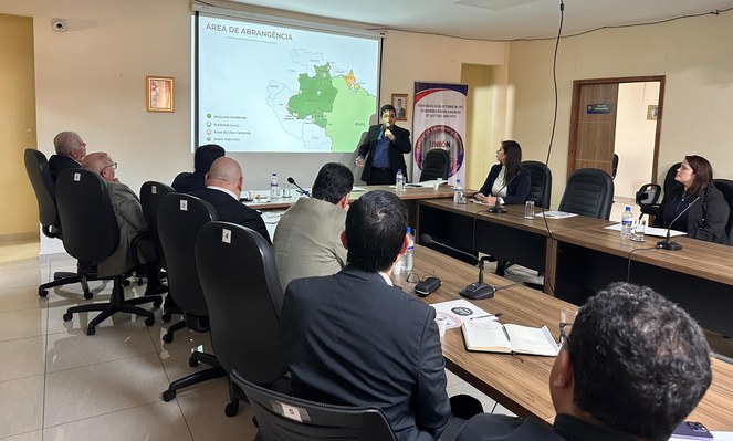 Foto mostra homem em pé com microfone na mão e um painel ao fundo