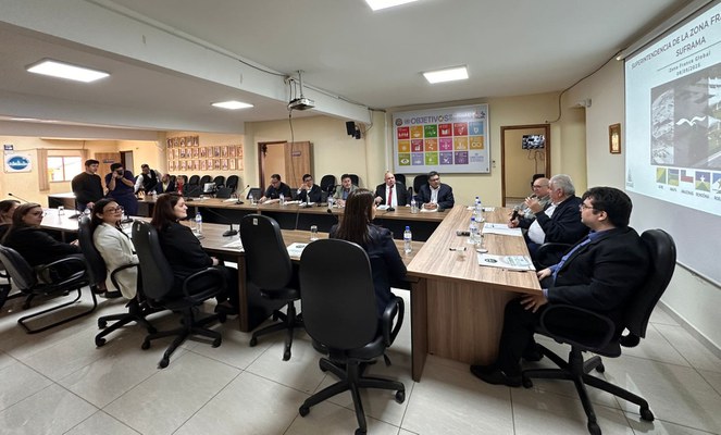 Foto mostra pessoas sentadas à mesa numa reunião