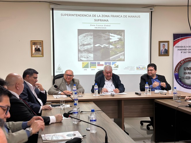 Foto mostra pessoas numa reunião com um painel ao fundo