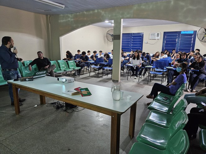 Foto mostra homem de blusa azul falando a grupo de estudantes
