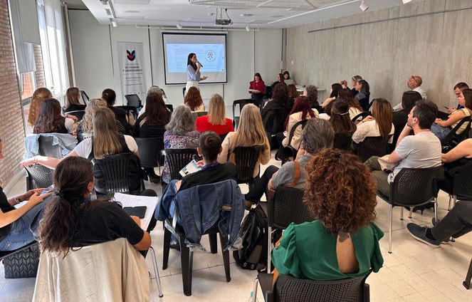 Foto mostra uma mulher em pé e microfone na mão falando a um grupo de outras mulheres sentadas