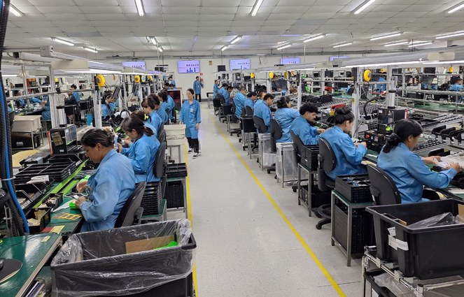 Foto mostra pessoas de bata azul em uma linha de produção fabril