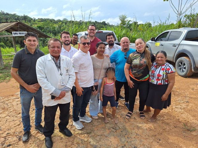 Foto mostra grupo de pessoas posando para foto, com carro ao fundo