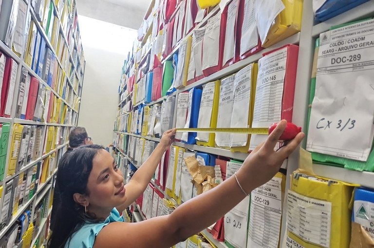 Foto mostra mulher com um trena na mão fazendo medição de caixas documentais