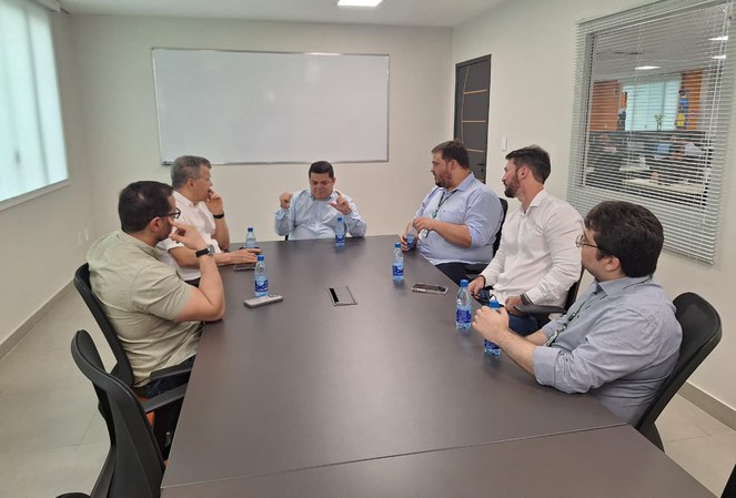 Foto mostra homem ao centro da mesa falando e gesticulando