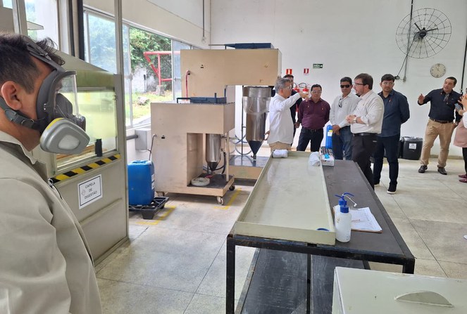 Foto mostra homem com máscara de proteção e outras pessoas conversando dentro de uma sala