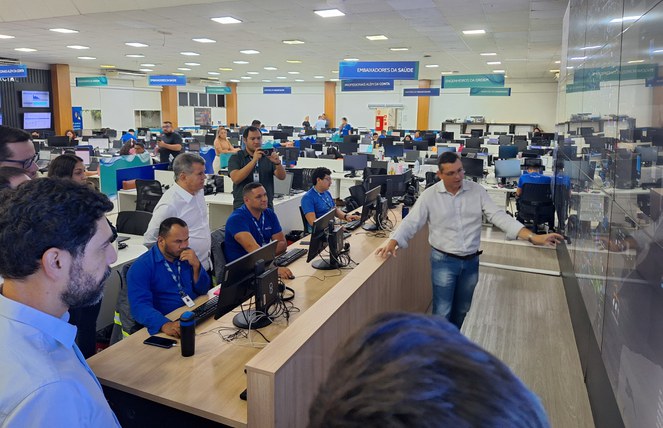 Foto mostra pessoas olhando para um painel eletrônico em uma empresa