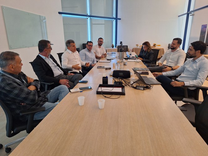 Foto mostra pessoas reunidas sentadas e diante de uma grande mesa