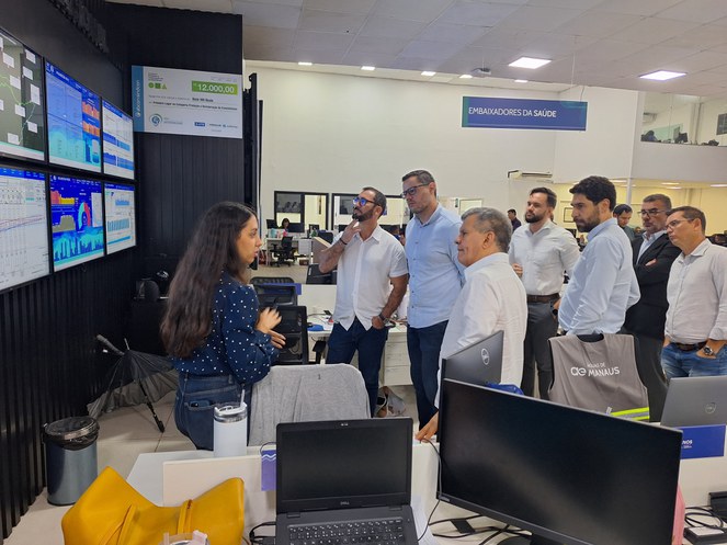 Foto mostra mulher fazendo uma explicação sobre informações expostas num grande painel eletrônico