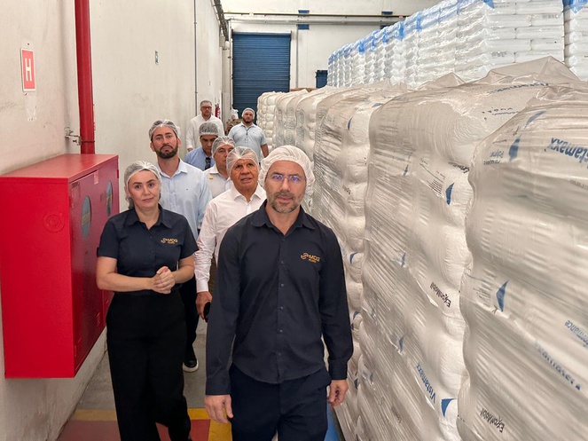 Foto mostra pessoas de touca branca andando em corredor cercado de sacos plásticos