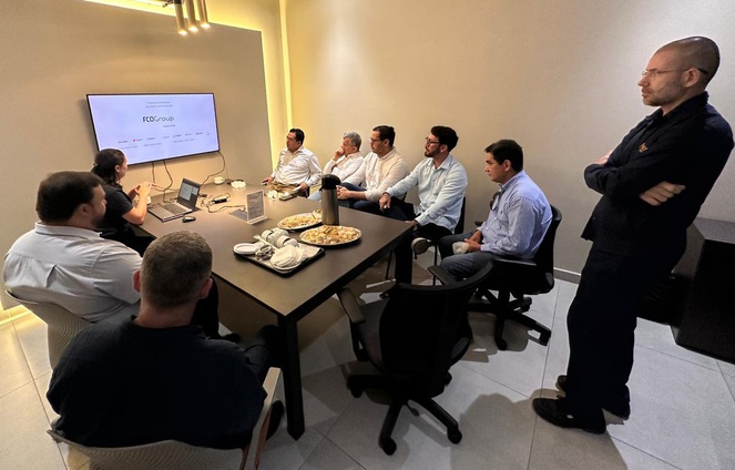 Foto mostra mulher fazendo uma explanação com o apoio de um telão, a um grupo de pessoas