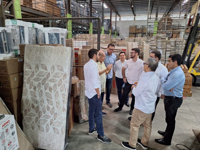 Foto mostra grupo de homens em uma fábrica cercado de caixas