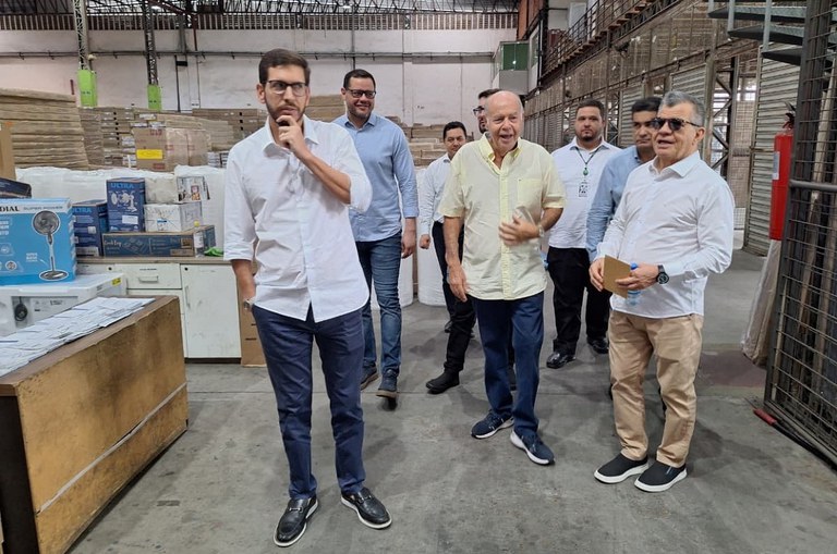 Foto mostra pessoas dentro de uma fábrica cercadas de caixas