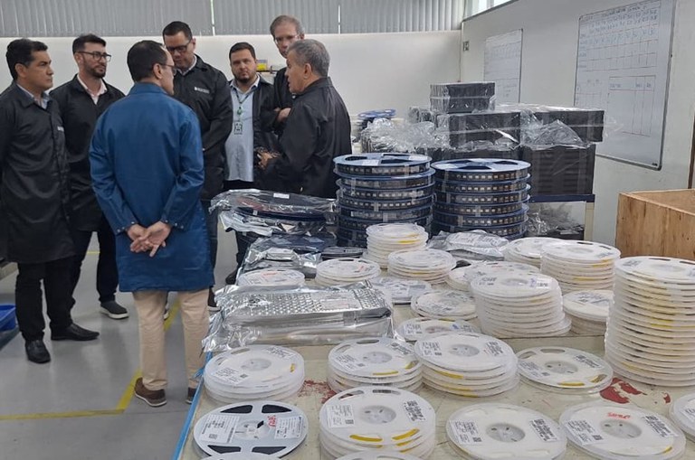 Foto mostra homens de bata conversando em frente a itens do mercado de informática 