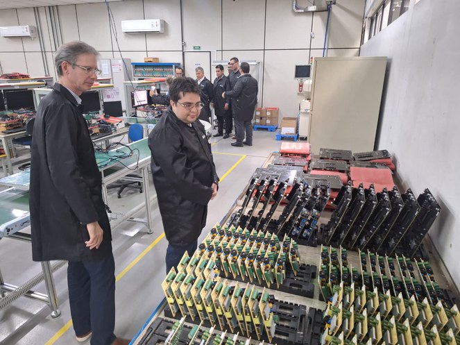 Foto mostra homens de bata preta olhando para itens de informática