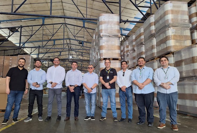 Foto mostra homens em volta de produtos plásticos numa fábrica