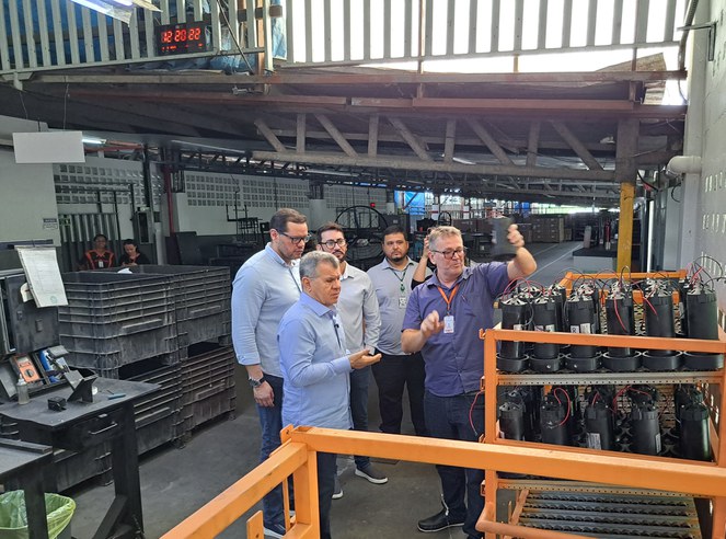 Foto mostra homem segurando uma peça observado por outro homem