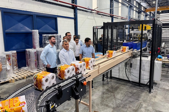 Foto mostra homens conhecendo uma linha de produção de papel higiênico